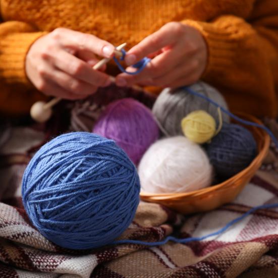 Garnnøgler og hænder der strikker.