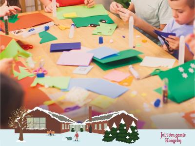 Børn sidder omkring bord og laver kreativt pynt. I bunden en illustration af et sneklædt Nyborg Bibliotek samt ordene "Jul i den gamle kongeby"