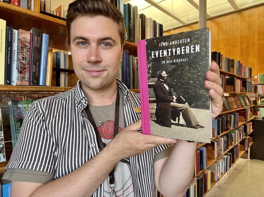 Bibliotekar Mathias Lyngs står og holder bogen "Eventyreren" på Nyborg Bibliotek.